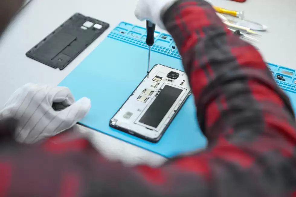 technician-wearing-white-antistatic-gloves-plaid-shirt-sitting-his-desk-using-precision-screwdriver-remove-screws-back-faulty-mobile-phone
