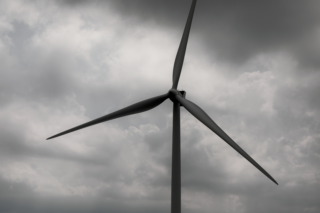 A wind turbine stands tall against a backdrop of dark, stormy clouds, symbolizing renewable energy.