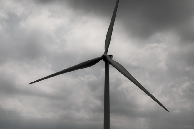 A wind turbine stands tall against a backdrop of dark, stormy clouds, symbolizing renewable energy.